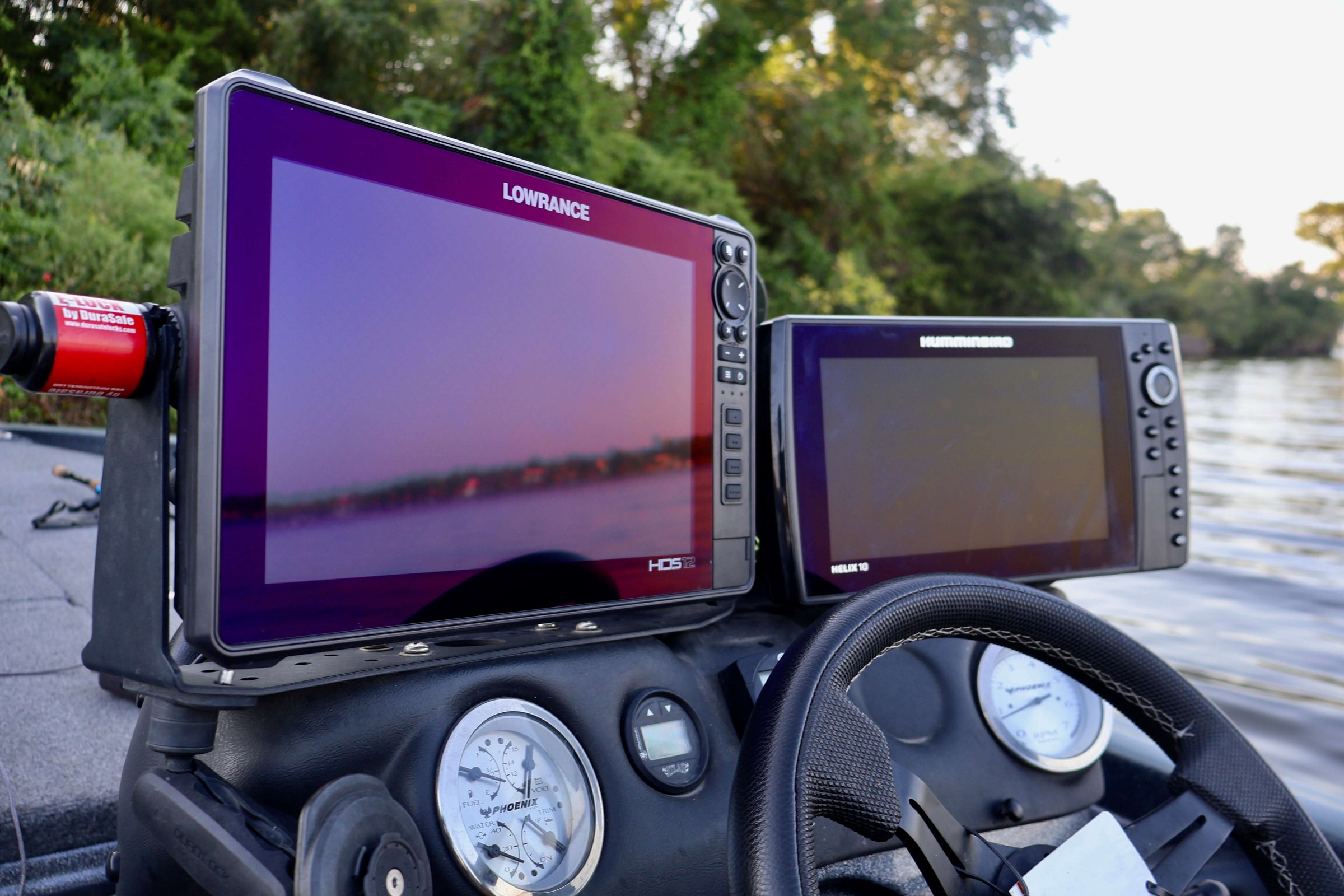 "Boat dashboard with modern fish finder and navigation screens on a river, surrounded by lush greenery."