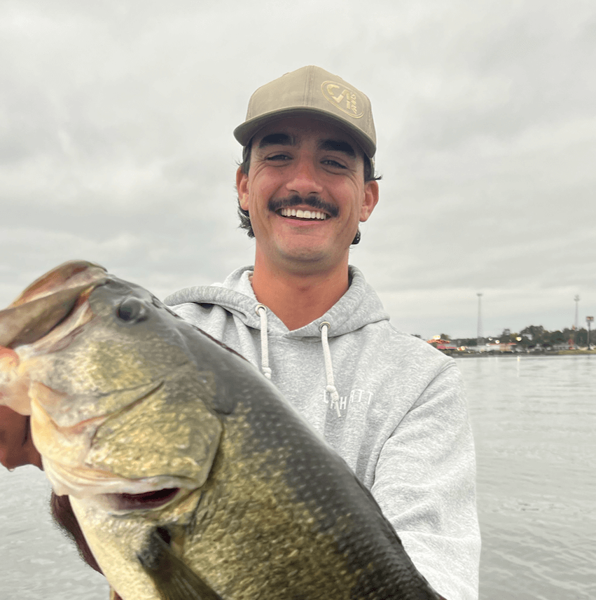 Person holding a large fish on a lake with a cloudy sky in the background.