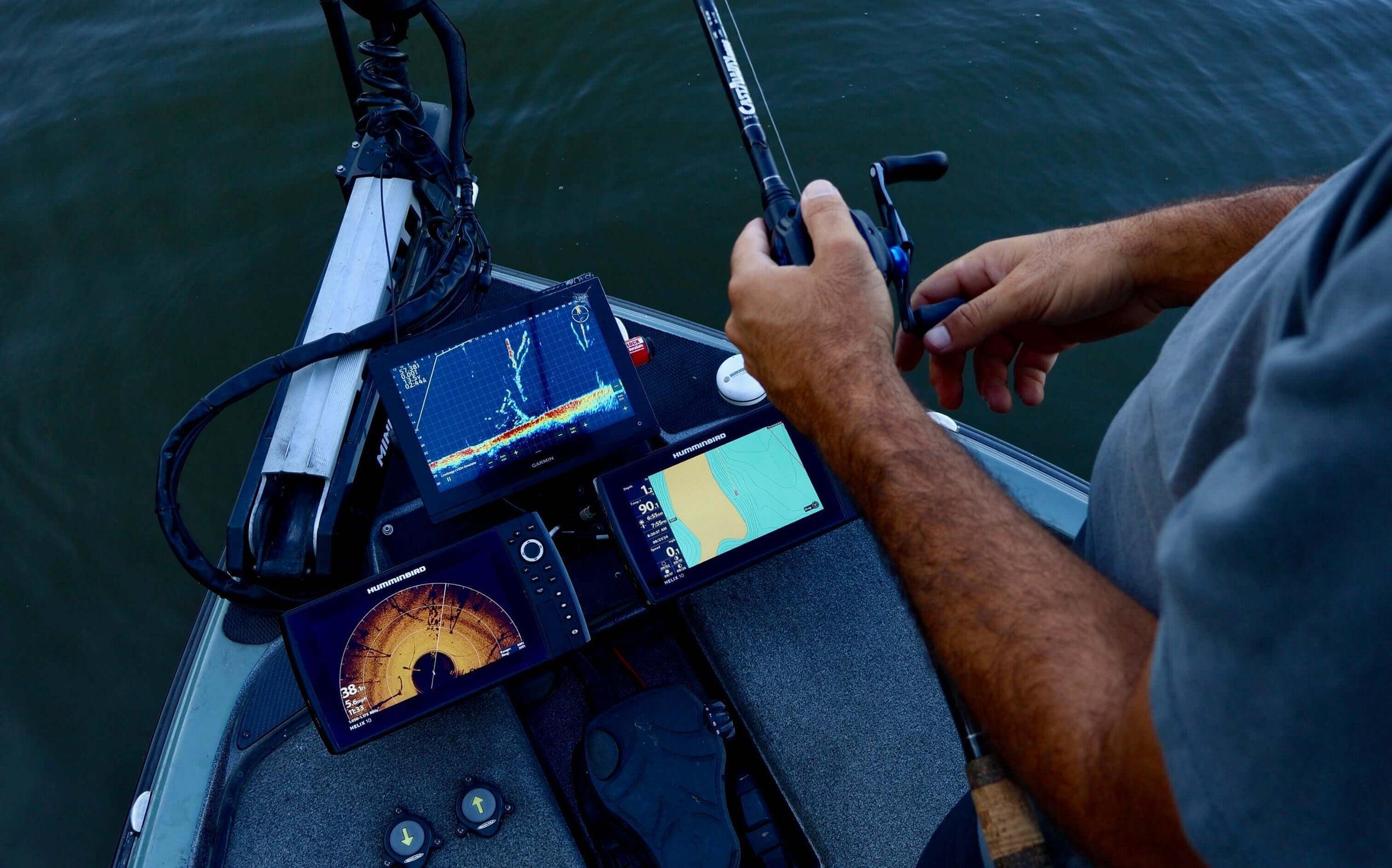 Angler using advanced fish finder technology on a boat at sea, showcasing digital screens with sonar and mapping features.