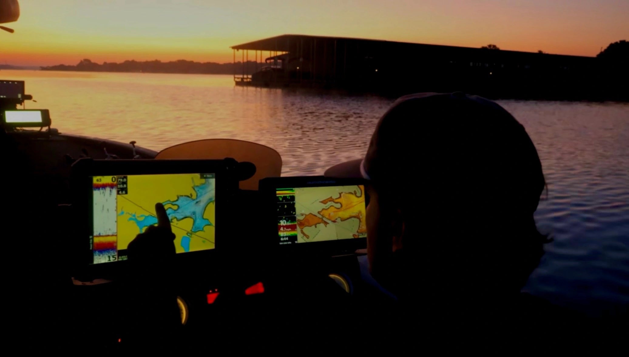 Person using a smartphone with a fishing app on a boat at sunset